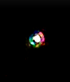Nighttime photo of a small multicolored orb of light with a bright white center against a dark background
