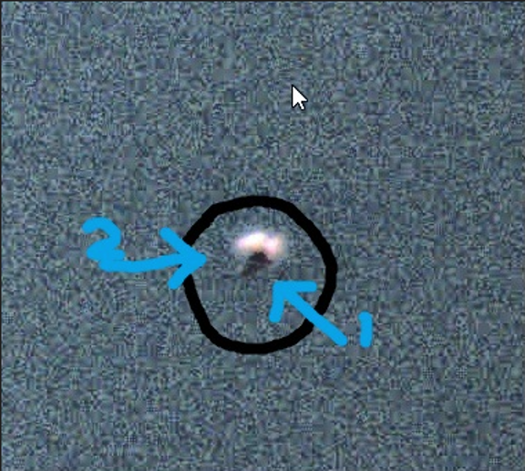 Grainy nighttime surveillance frame with a small bright anomaly circled and labeled with directional arrows